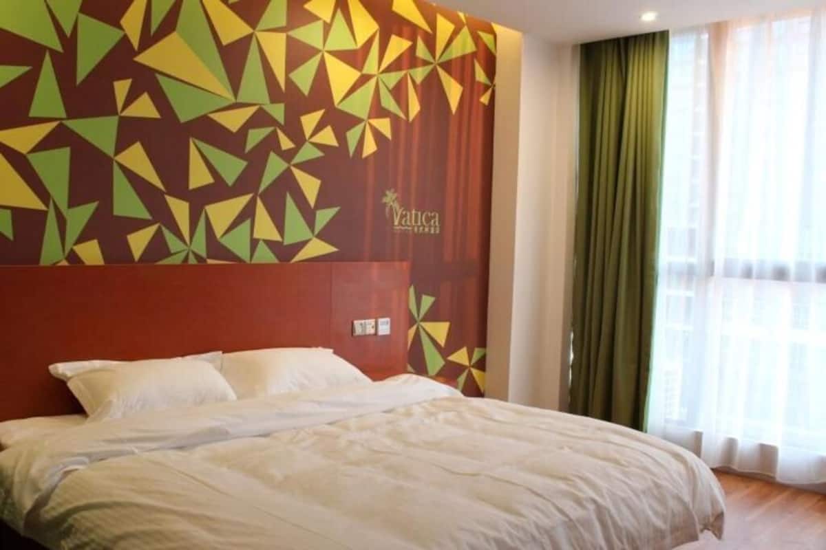 Quarto de hotel com uma cama, um design geométrico na parede e uma janela com cortinas.