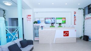 Egy szállodai recepciós tér, amelyben található egy recepciós pult, két recepciós, egy hűtőszekrény, egy kék színű lépcsőház és egy kanapé.