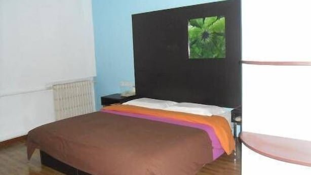 Ein Schlafzimmer mit Bett, Nachttisch, Fenster mit Pflanze und Heizkörper.