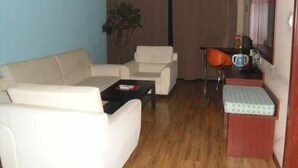 Ein Wohnzimmer mit einer Couch, einem Couchtisch, einem kleinen Tisch mit Wasserkocher und einem Sessel.