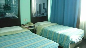 Ein Hotelzimmer mit zwei Betten, einem Nachttisch, einem gerahmten Bild an der Wand und einem Fenster mit Vorhängen.