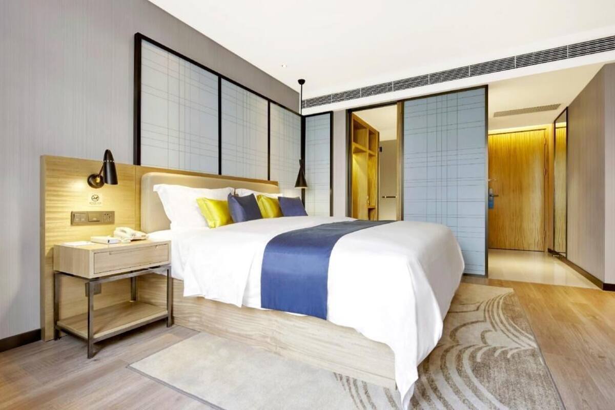 A modern hotel room with a large bed, bedside table, and a view of the hallway.