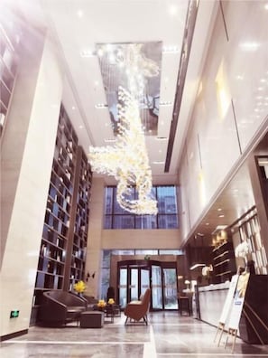 A spacious lobby with a modern chandelier, seating area, and a reception desk.