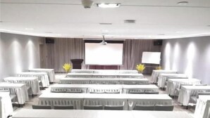 Un salón de conferencias con mesas, sillas, un atril y una pantalla grande.