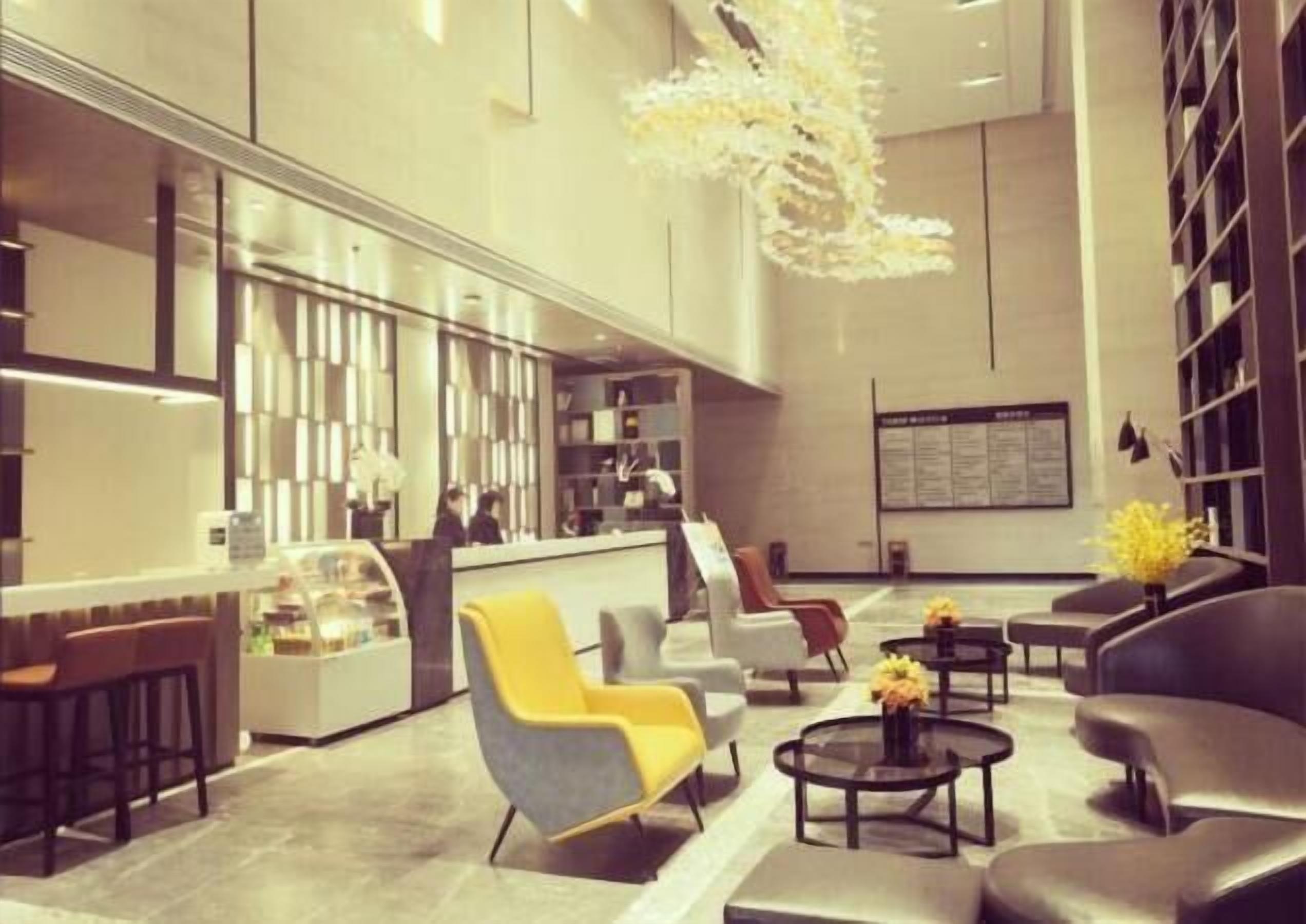 A modern lobby with a reception desk, seating area, and a large chandelier.