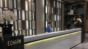 Un mostrador de recepción con base de mármol identificado con 'ECHARM', diseño moderno con paneles de luz verticales, y una persona de pie detrás del mostrador.