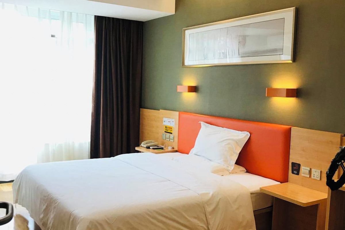Et hotelværelse med en seng, et natbord og en lampe på væggen.