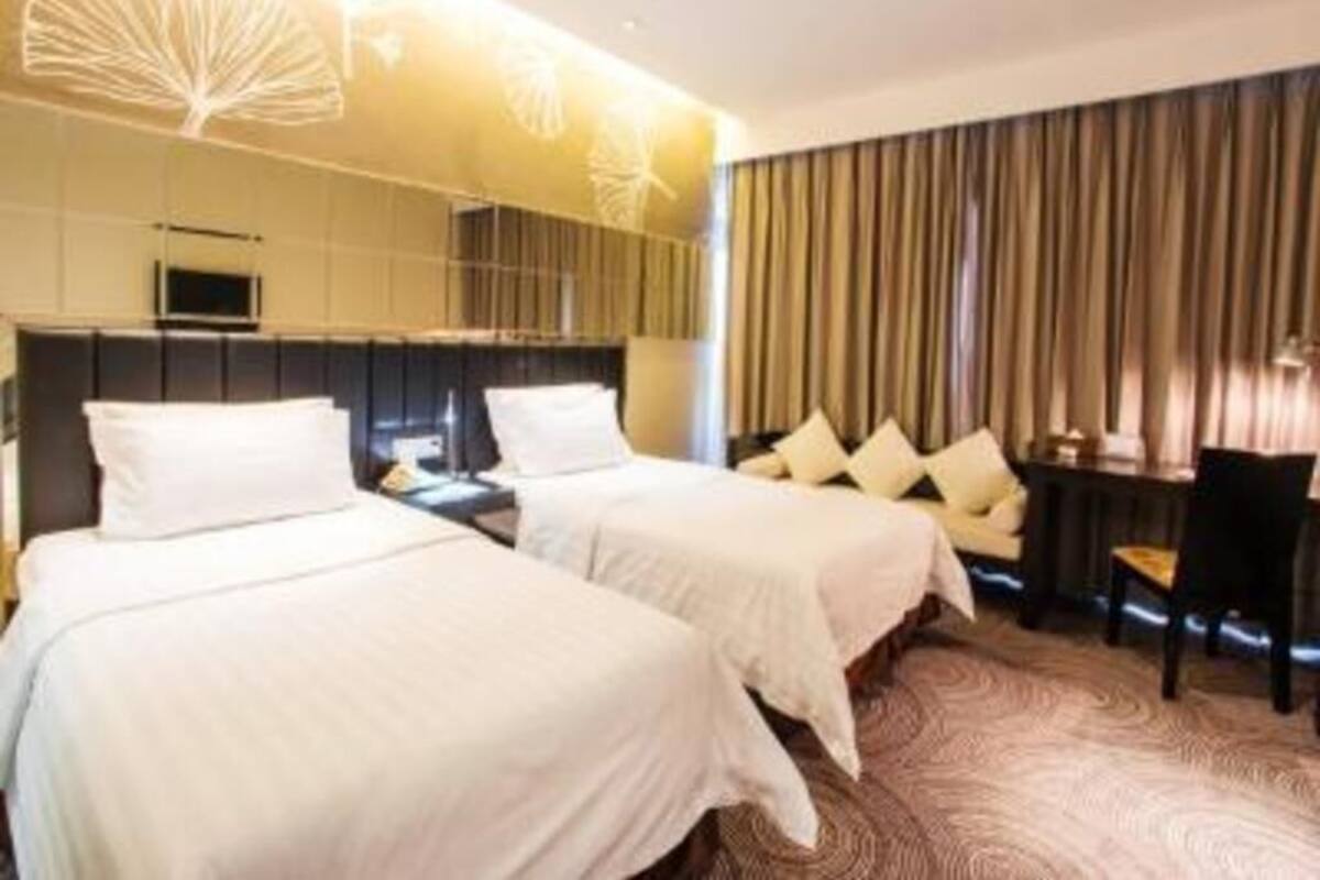 A hotel room with two beds, a desk, and a large window with curtains.