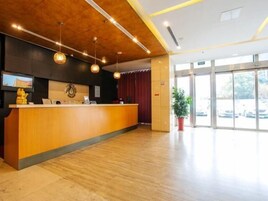 Un mostrador de recepción con superficie de madera, luces colgantes tipo lámpara, un reloj y una planta.