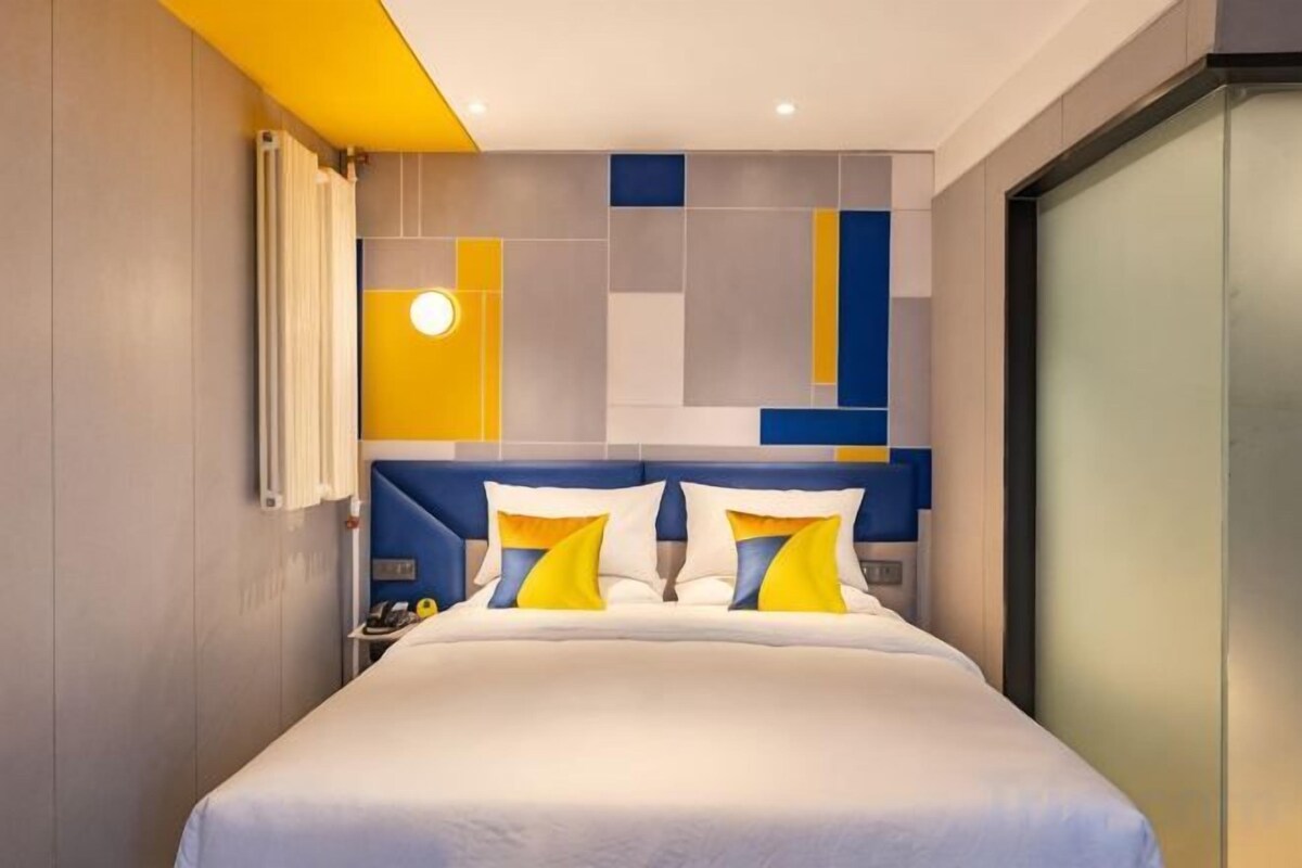 A modern hotel room with a large bed, a headboard with geometric patterns, and a nightstand with a lamp.