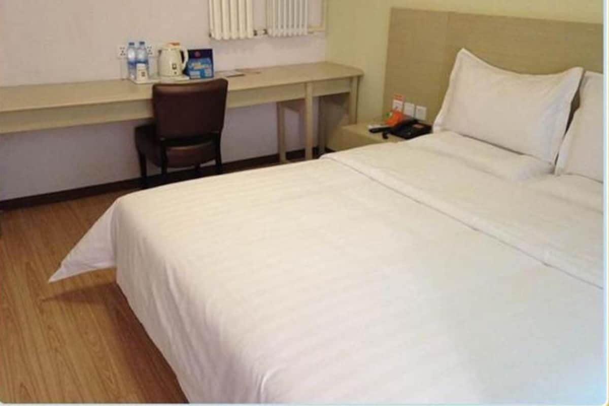 Ein Hotelzimmer mit Bett, Schreibtisch, Stuhl, Nachttisch und einem Fenster mit Jalousien.