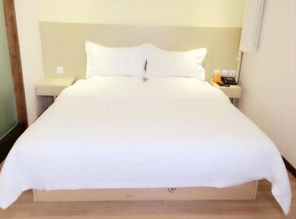 A neatly made bed with white linens, a wooden headboard, and a nightstand with a lamp and a bottle. - 7days Inn Chain Hotel (Beijing)