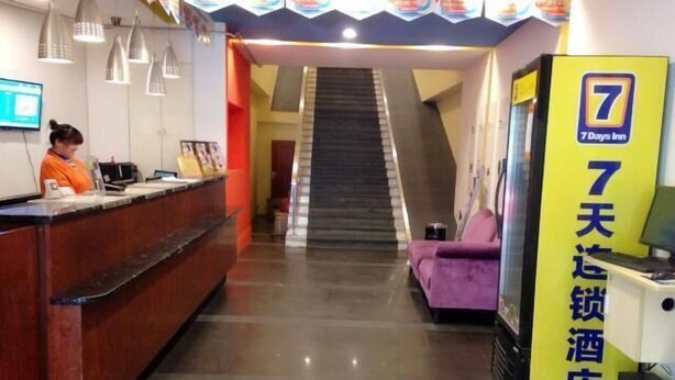 Zona de recepción de un hotel, con mostrador de recepción, una escalera y un cartel con el nombre del hotel.