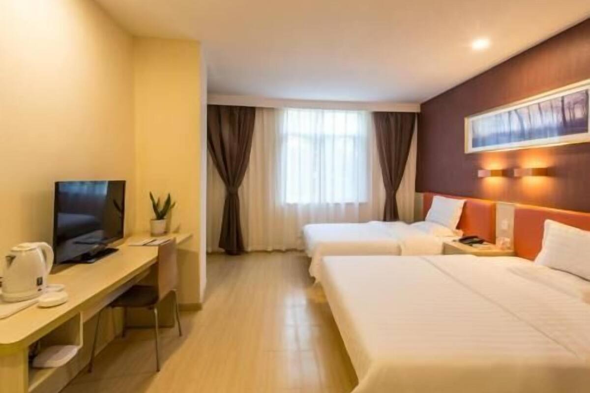 A hotel room with a desk, two beds, a TV, and a window with curtains.