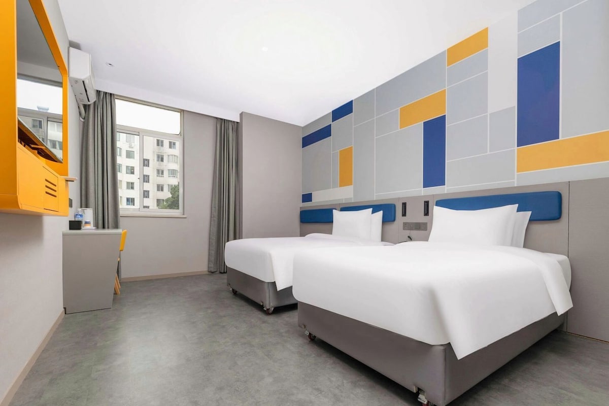 Une chambre d’hôtel avec deux lits, un bureau et une fenêtre avec des rideaux.