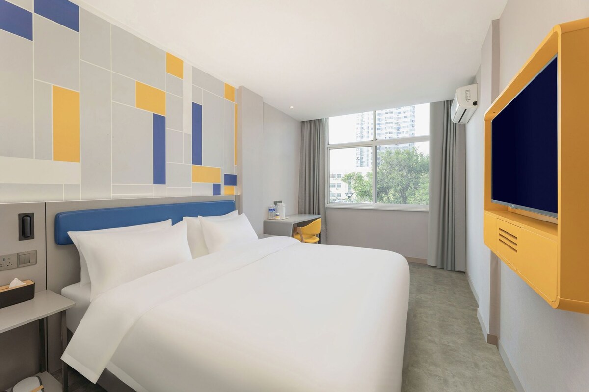 Une chambre d’hôtel avec un lit, un bureau, une chaise, une télévision et une fenêtre avec des rideaux.