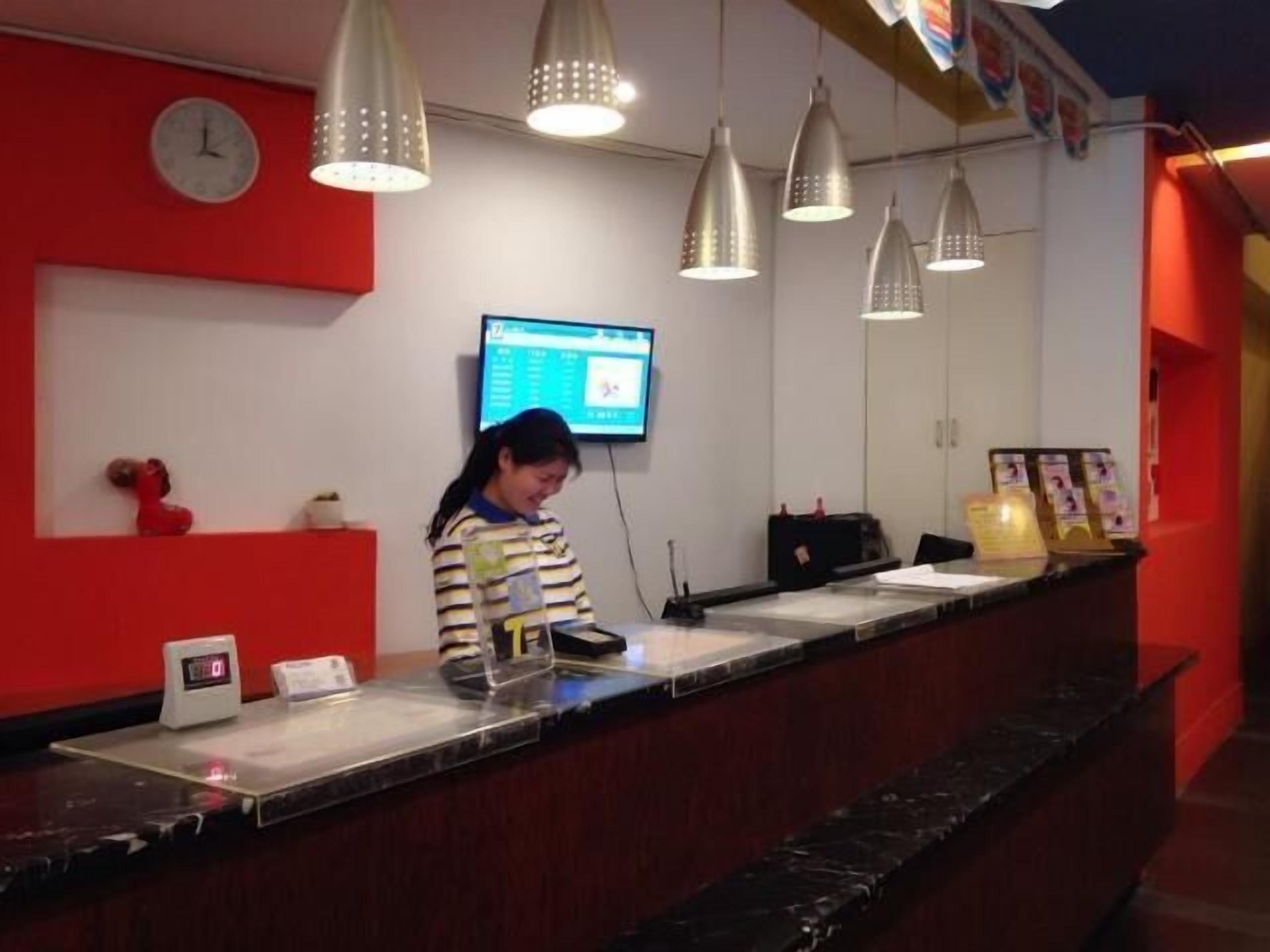 A reception desk with a digital clock, a television screen, and hanging pendant lights.