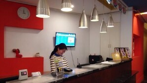 Un mostrador de recepción con un reloj digital, una pantalla de televisión y lámparas colgantes.