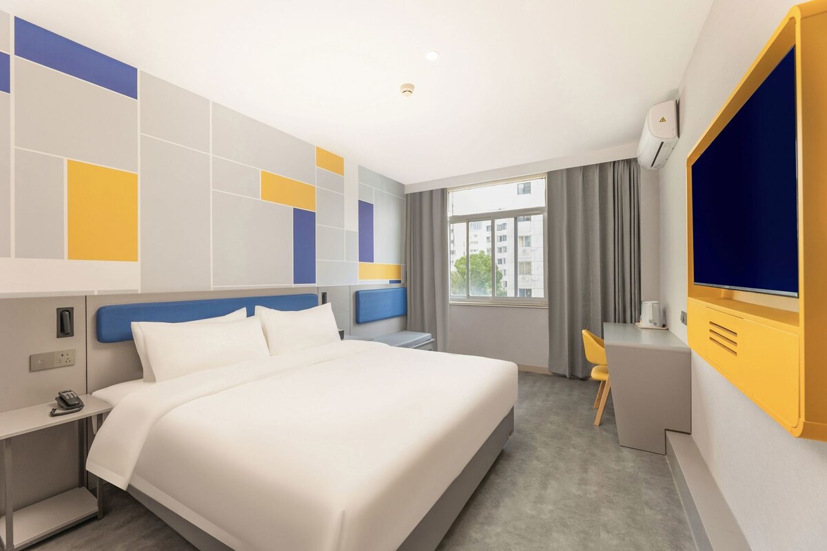 Une chambre d’hôtel avec un grand lit, un bureau, une chaise, une télévision et une fenêtre avec des rideaux.