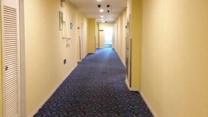Un pasillo de hotel con alfombra estampada, puertas a ambos lados y un techo con iluminación empotrada.