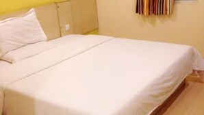 Habitación individual con cama de una sola plaza, piso de madera, cubrecama blanco sencillo y cabecera simple.