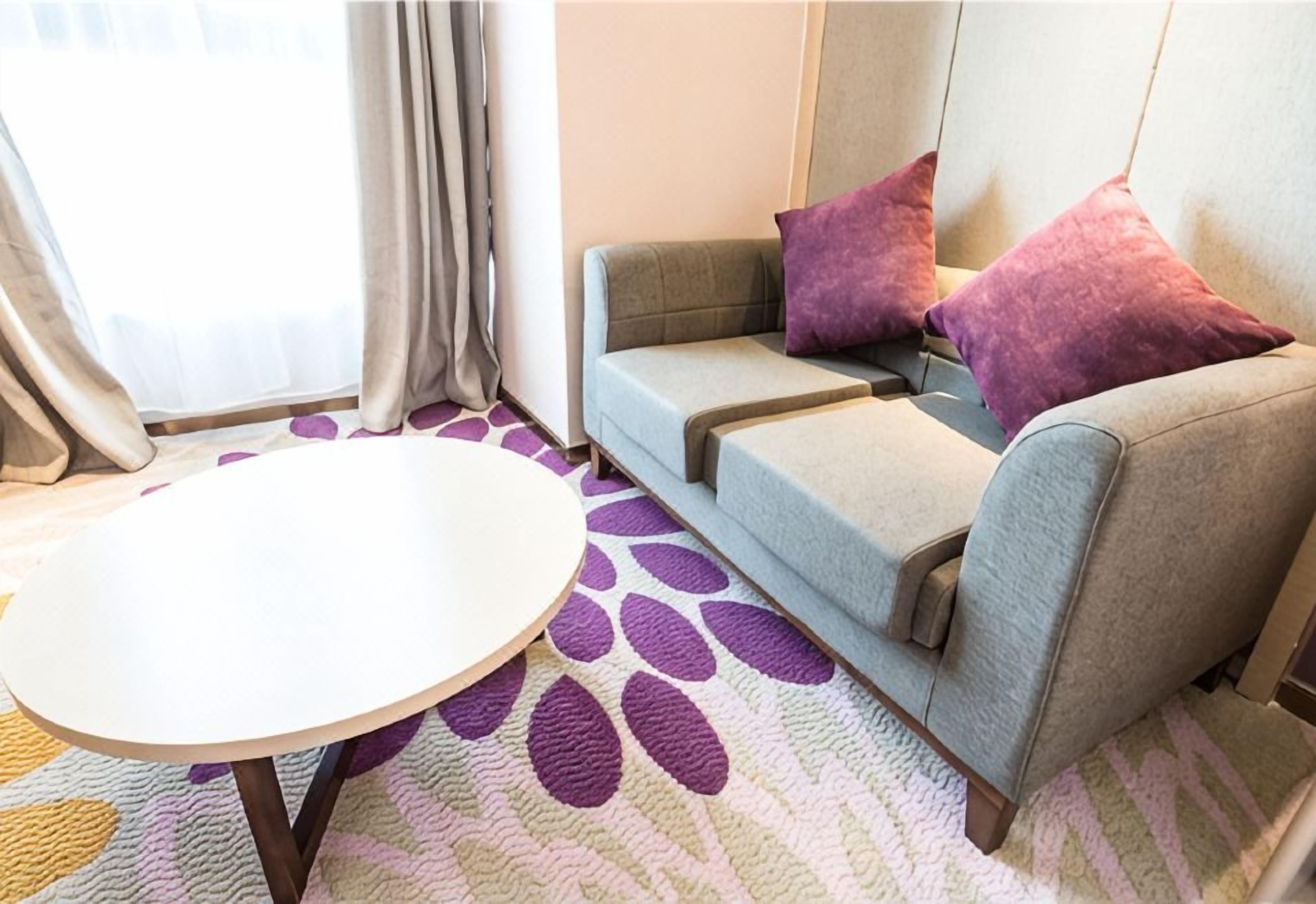 Ein Zimmer mit einer Couch, zwei Kissen, einem runden Tisch und einem gemusterten Teppich.