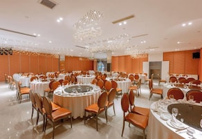 Uma sala de banquetes com mesas redondas, cadeiras e um lustre decorativo central.