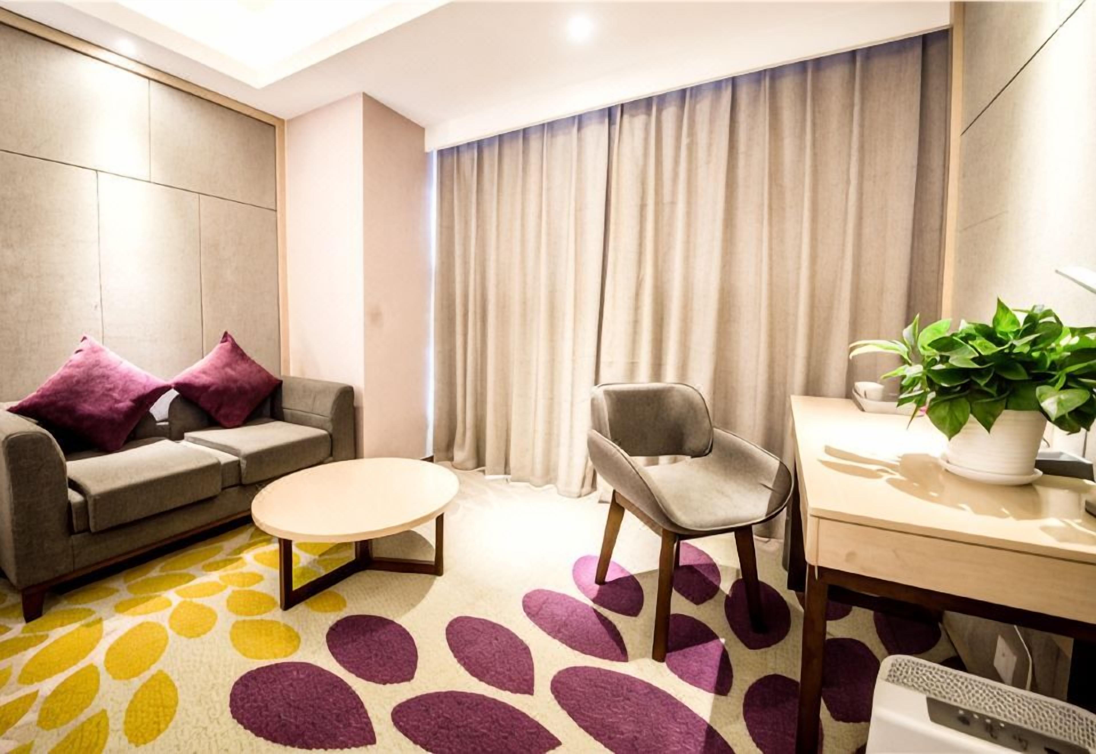 Habitación de hotel moderna con sofá, sillón, mesa redonda de centro y escritorio con planta.