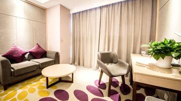 Habitación de hotel moderna con sofá, sillón, mesa redonda de centro y escritorio con planta.