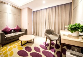 Habitación de hotel moderna con sofá, sillón, mesa redonda de centro y escritorio con planta.