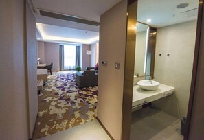 A hotel room with a modern bathroom, a sofa, and a patterned carpet.