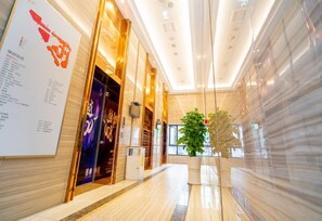 Un vestíbulo moderno de hotel con piso de mármol, un mostrador de recepción y una planta grande en maceta.