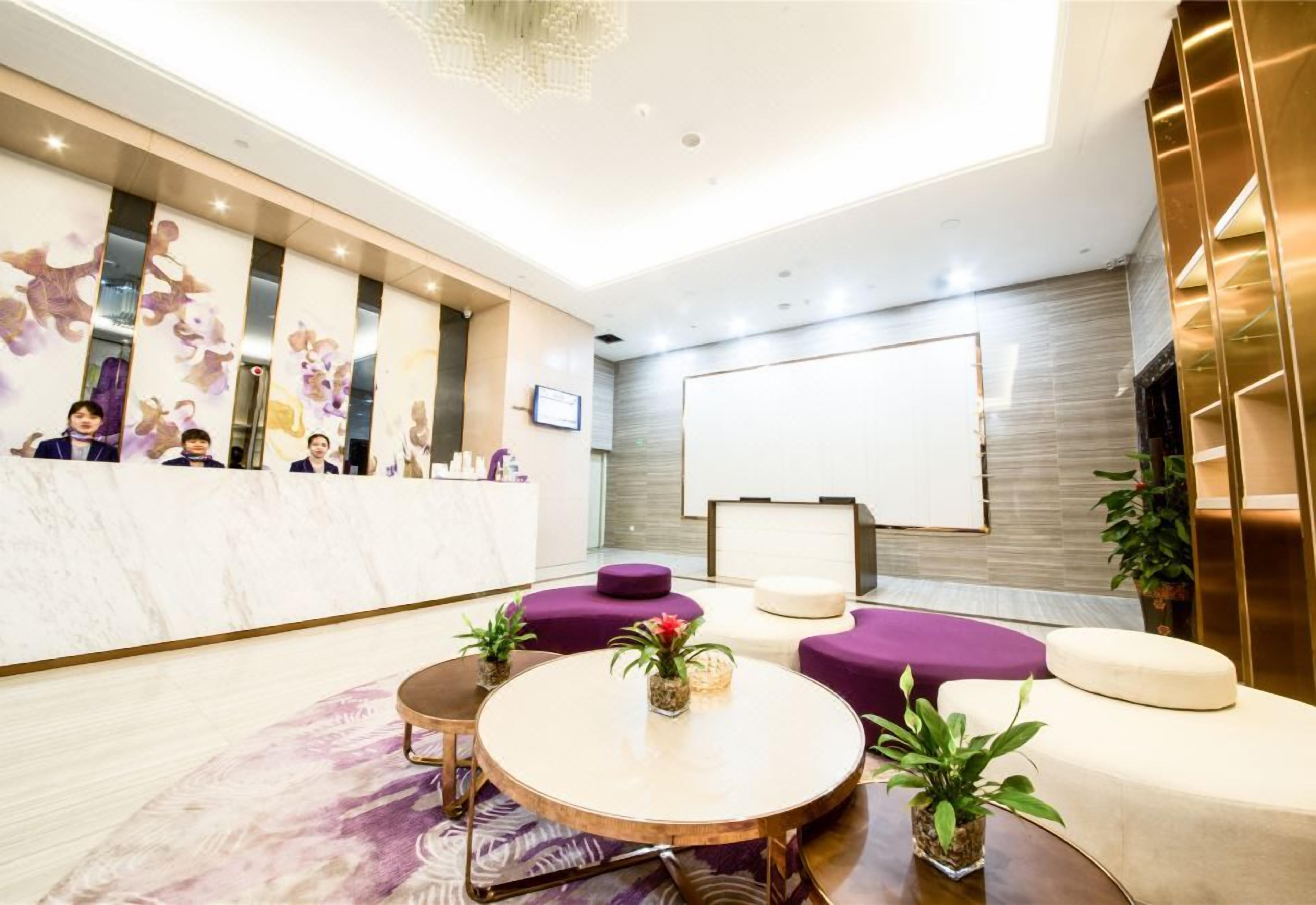 Un espace d’accueil moderne avec un comptoir en marbre, des sièges violets et un grand tableau blanc.