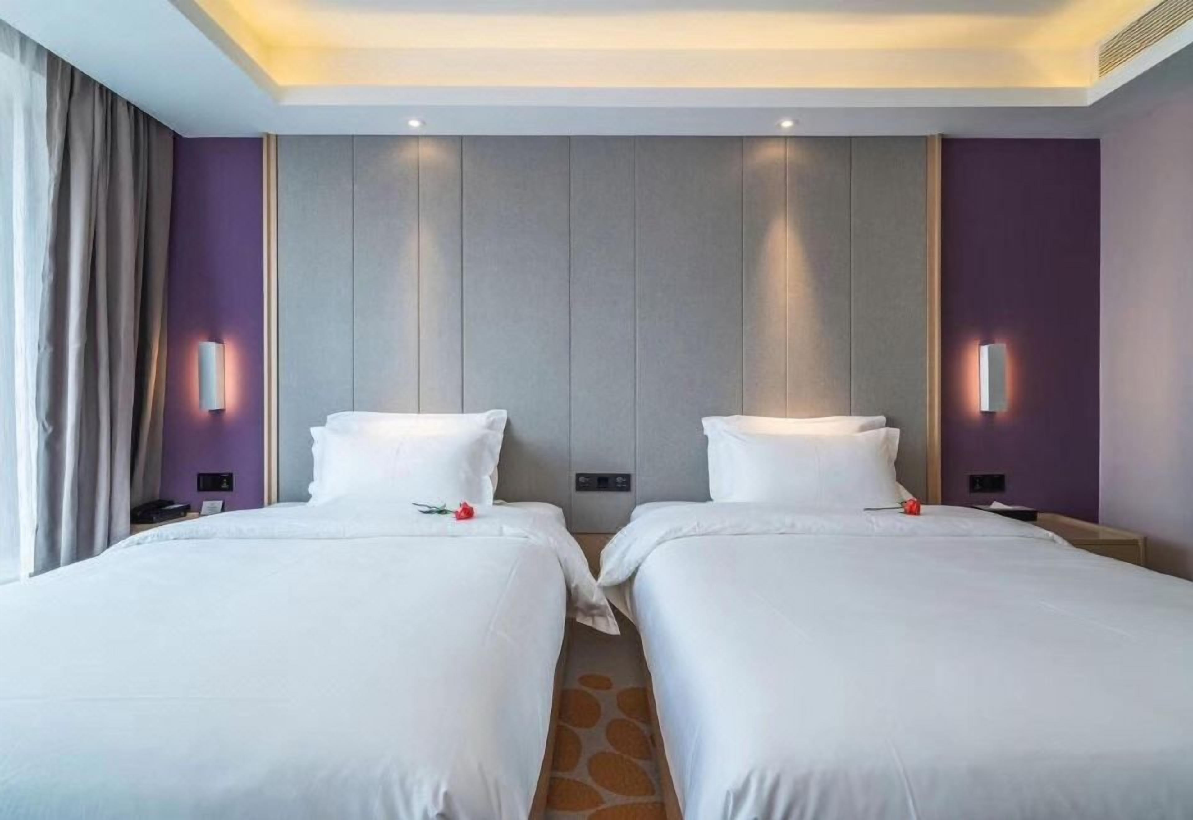 Camera d'albergo con due letti, un comodino, una lampada e un punto luce a parete.