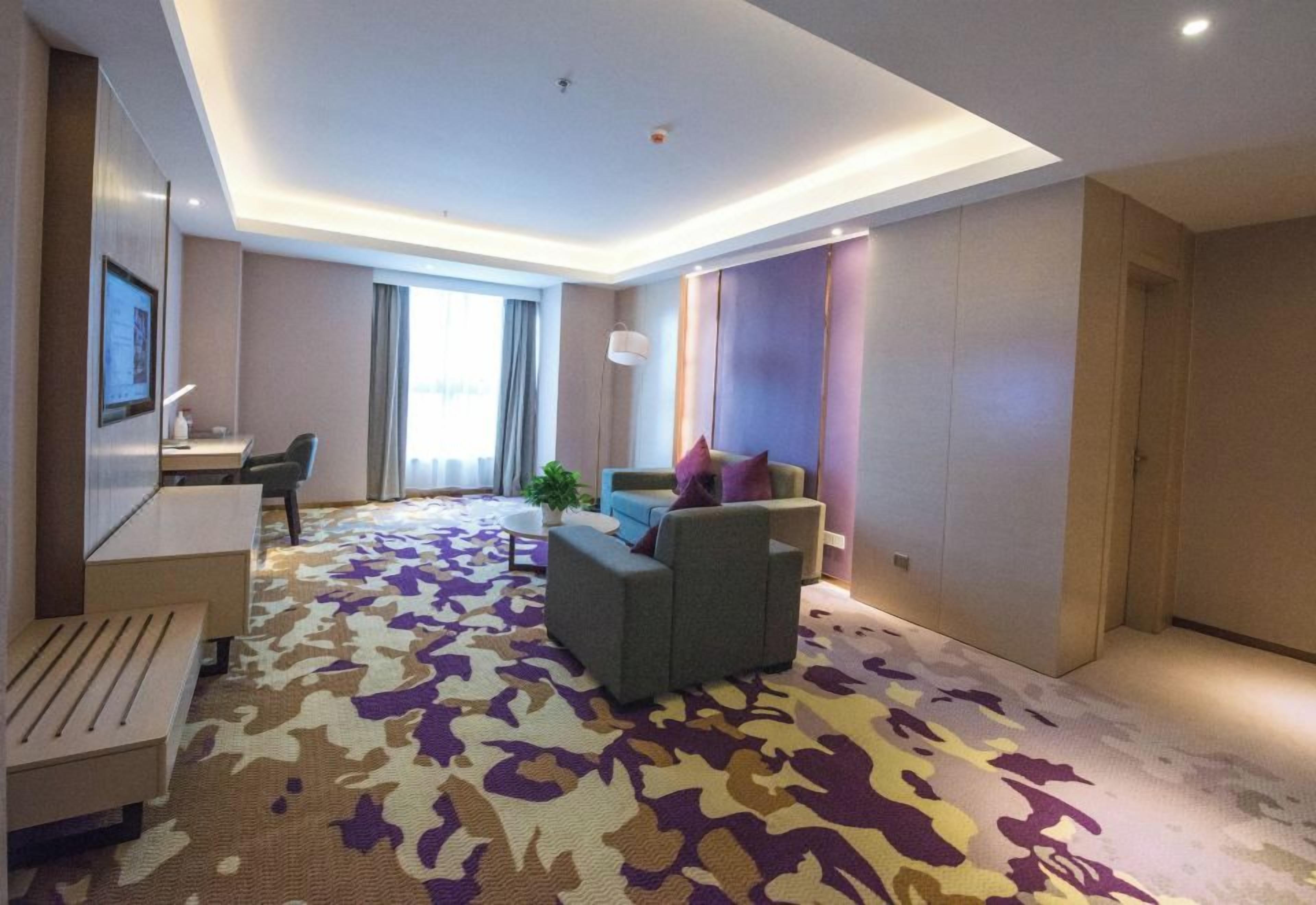 Une chambre d’hôtel moderne dotée d’une grande fenêtre, d’un canapé, d’un bureau et d’un tapis à motifs.
