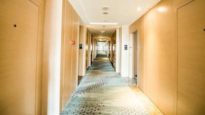 En hotellkorridor med träpanel på väggarna, ett mönstrat golv och en lång gång som leder till dörrar.