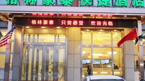 A hotel entrance with glass doors, a red awning, and two flags. - Greentree Inn Express (Dalian)