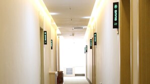 A hotel corridor with doors marked by green signs, a trash bin, and a vent on the wall. - Greentree Inn Express (Dalian)