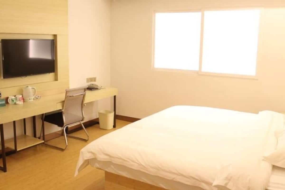 A hotel room with a bed, a desk with a chair, a television, and a window.