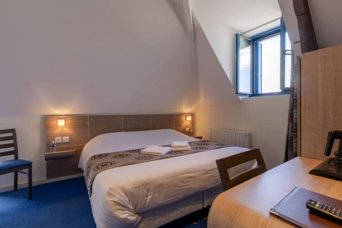 Une chambre d’hôtel avec un lit, une table de chevet, une chaise et une fenêtre.