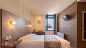 Una habitación de hotel con cama, mesita de noche, lámpara, televisión y una ventana con cortinas.