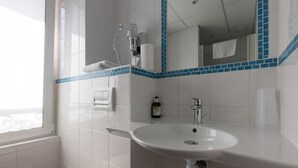 Un baño con un lavamanos blanco, un espejo y un perchero para toallas.