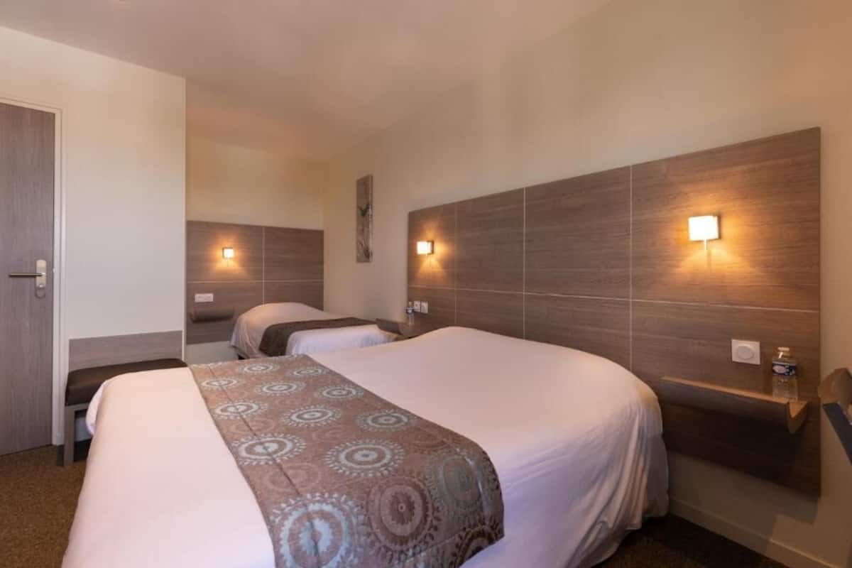 Une chambre d’hôtel avec deux lits, une tête de lit en bois, des lampes fixées au mur et un banc.