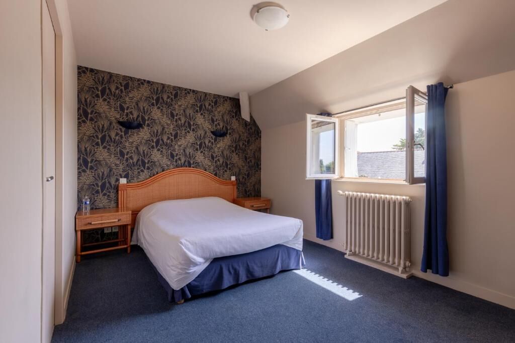 Un dormitorio con cama, mesita de noche, ventana con cortinas, radiador y pared con diseño.