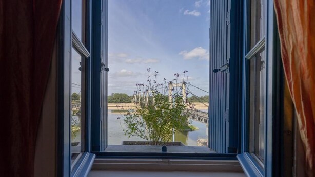 Una ventana con vista a un río, un puente y una planta en el alféizar.