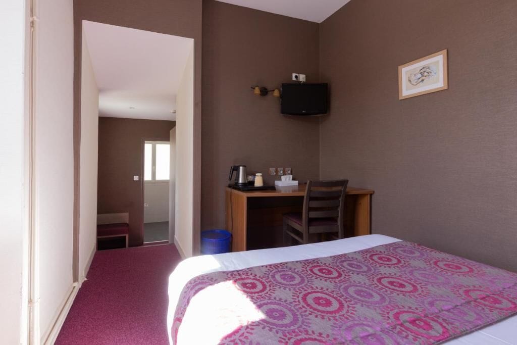 Ein Hotelzimmer mit einem Bett, einem Schreibtisch, einem Stuhl, einem Fernseher und einem gerahmten Bild an der Wand.