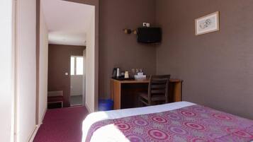 A hotel room with a bed, a desk, a chair, a television, and a framed picture on the wall.