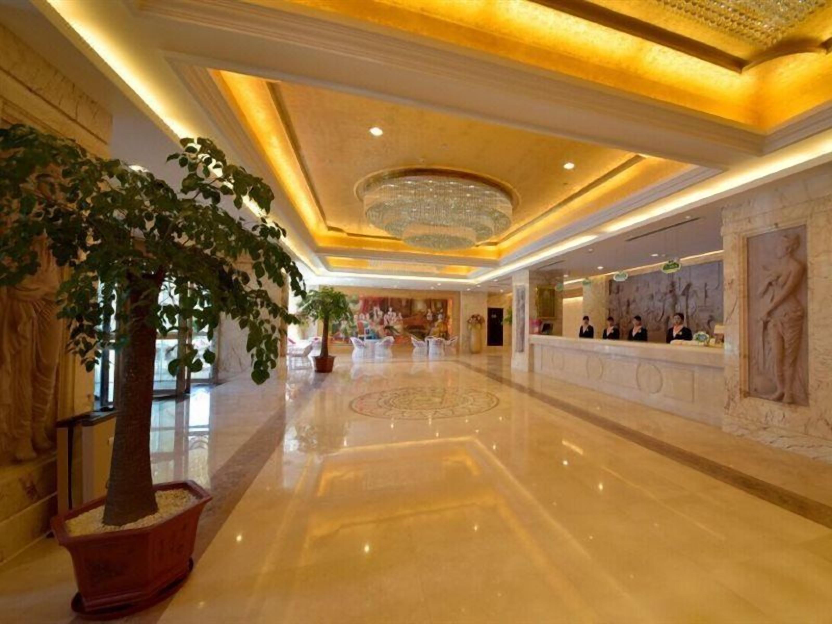 Un vestíbulo de hotel con piso de mármol pulido, una mesa de recepción y una gran araña.