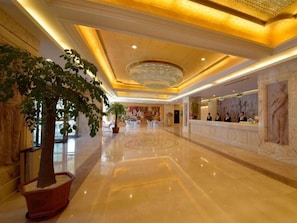 Un hall d’hôtel doté d’un sol en marbre poli, d’un comptoir de réception et d’un grand lustre.