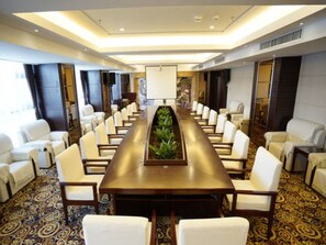 A conference room with a long table, white chairs, and a decorative plant centerpiece. - Vienna International Hotel (Zhumadian)